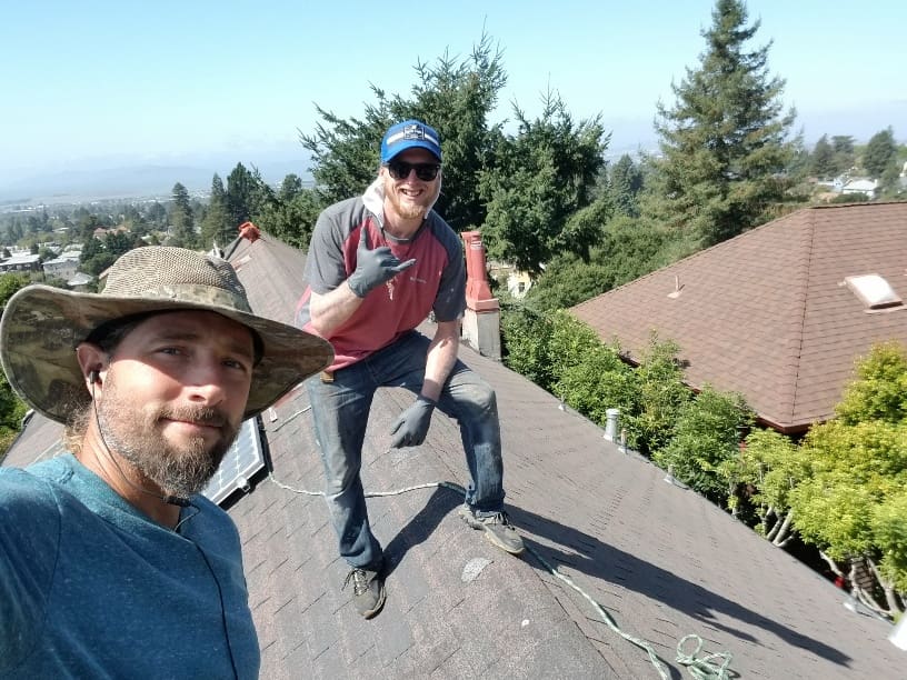Two men standing on a roof with trees in the background.
