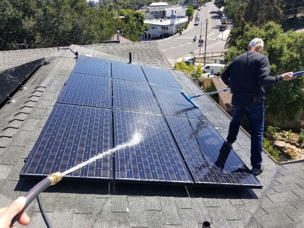 A man is cleaning the solar panels on the roof.