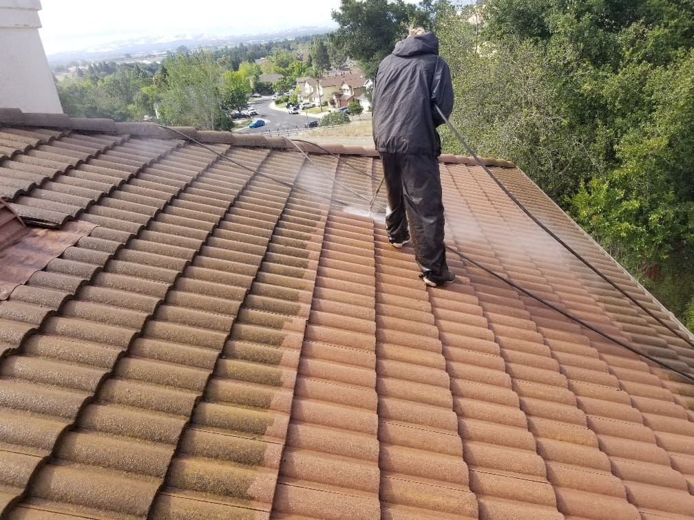 A man standing on top of a roof spraying water.