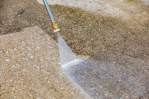 A person using a high pressure washer on the ground.