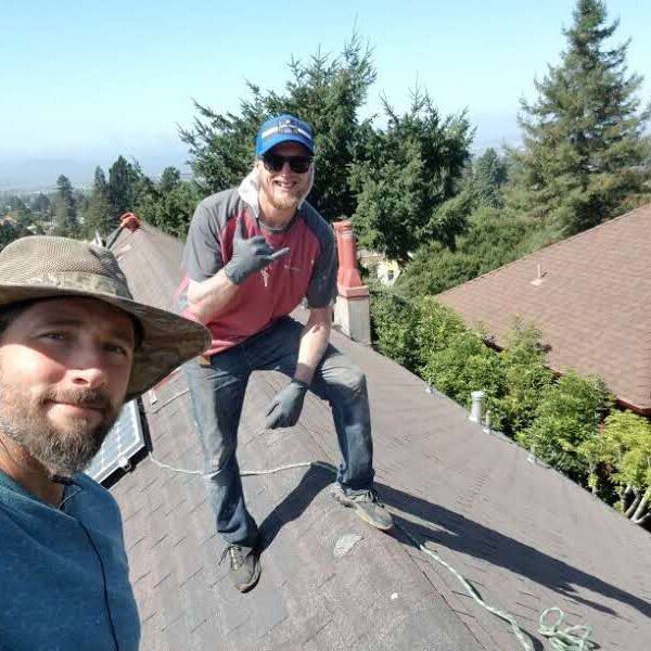 Two men standing on a roof with trees in the background.
