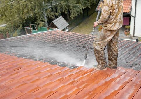 A man in camouflage suit cleaning the roof of a house.