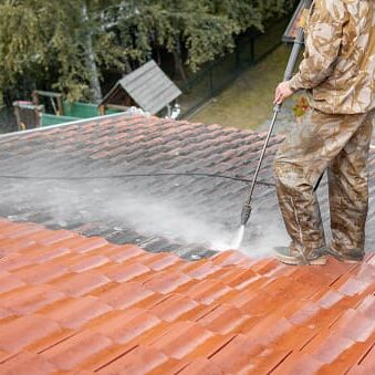 A man in camouflage suit cleaning the roof of a house.